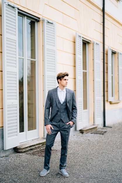 Serious groom looks into the distance and stands at the door of an old shuttered house