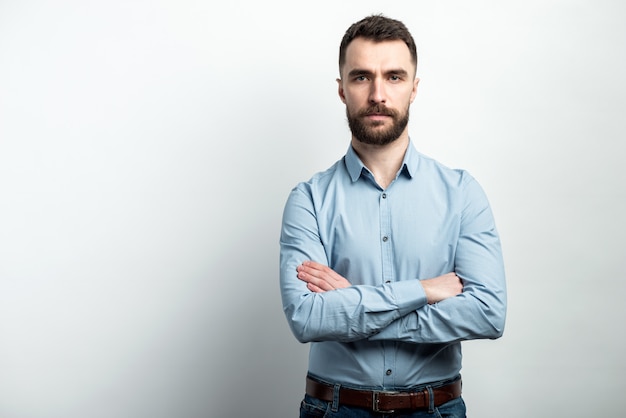 Serious guy in blue shirt stands folded hands and posing