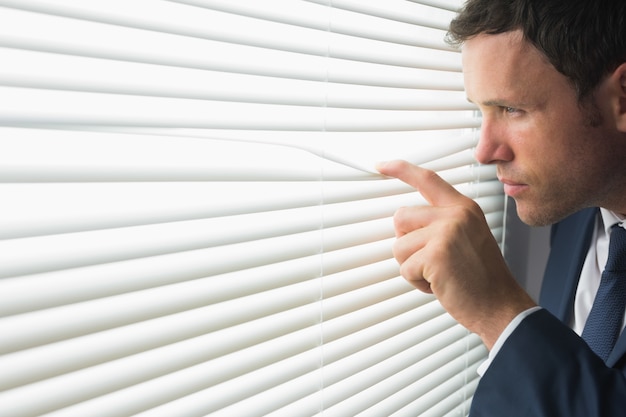 Photo serious handsome businessman looking through roller blind