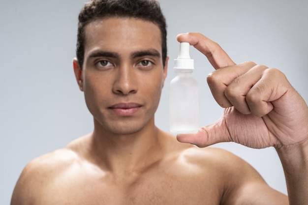 Serious handsome male holding a small bottle in his handd