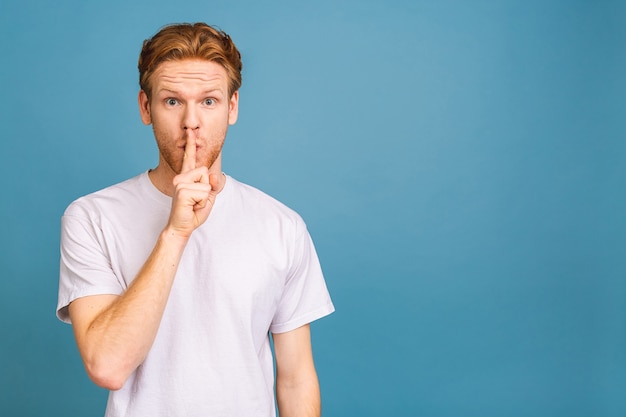 a serious handsome man keeps his front finger on his lips, tries to keep the conspiracy