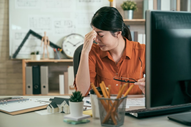 Serious hardworking unhappy woman architect engineer busy\
working on big project at construction office desk with desktop and\
building plans. female designer having headache and eyes painful\
tired.