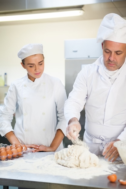 Serious head chef showing trainee how to prepare dough