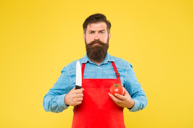 Фото Серьезный хипстер держит помидор и нож, чтобы приготовить свежую вегетарианскую пищу для здорового питания