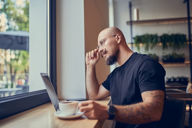 진지한 힙스터 밀레니엄 남성은 커피 프리랜서 컨셉으로 카페에 앉아 노트북 작업을 합니다.