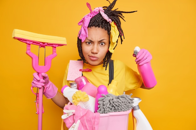 Serious housekeeper with dreadlocks holds chemical detergent and mop