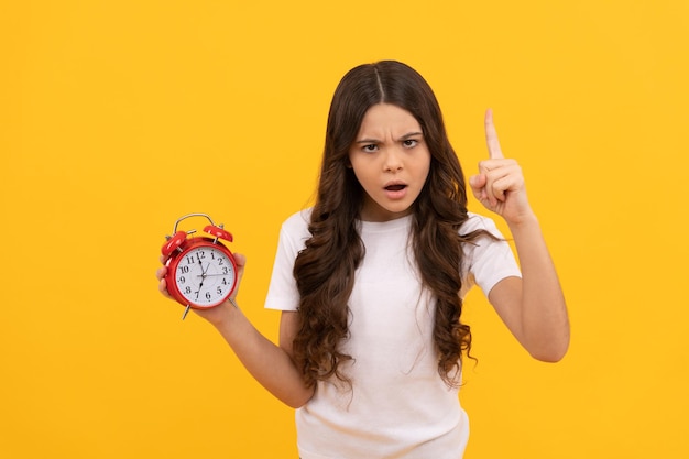 Il bambino serio tiene la sveglia retrò che mostra l'ora con la disciplina del dito alzato