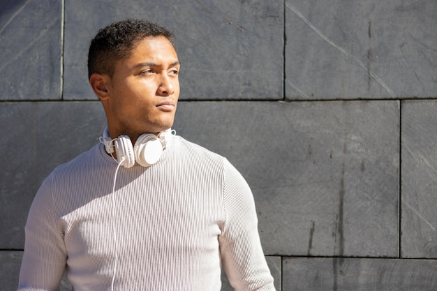 Serious Latin man with headphones on a gray wall background