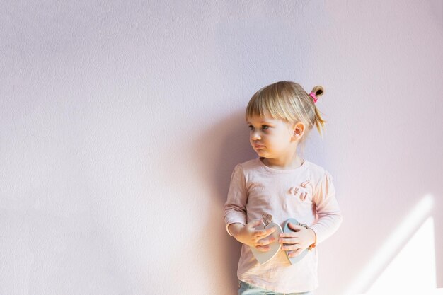 A serious little girl holds two wooden white hearts in her hands It is thoughtful and serious