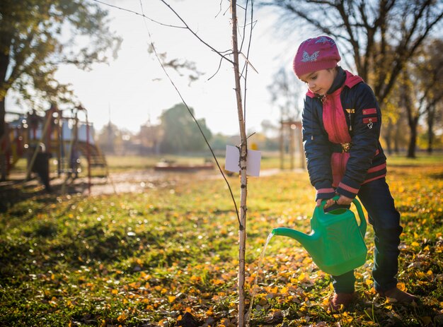 Серьезная трудолюбивая девочка поливает посадившее дерево