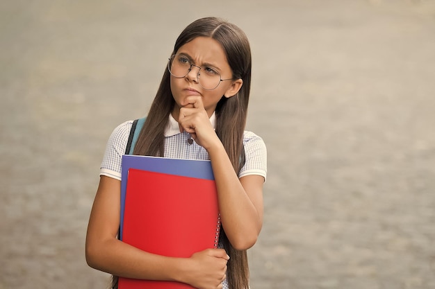 Serious little kid in glasses hold school books with thoughtful look outdoors imagination