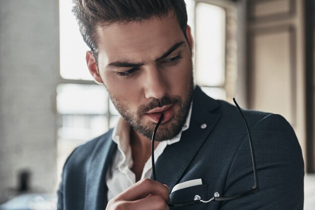 Serious look. Thoughtful young man in full suit looking down while spending time at home