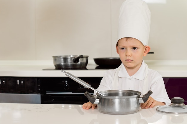 Serious looking little chef wearing a toque standing in the kitchen