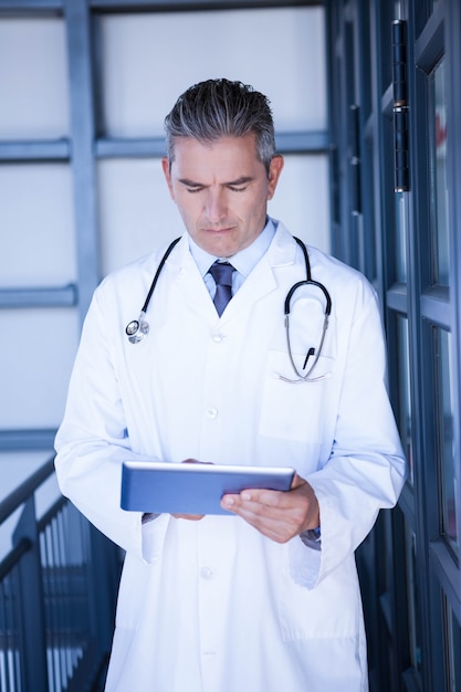 Серьезный мужской доктор используя цифровую таблетку в больнице