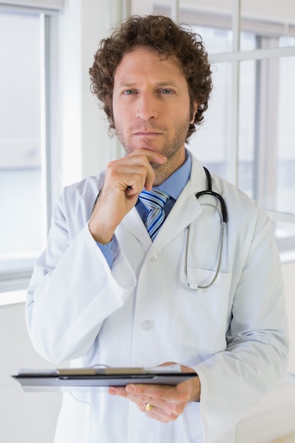 Serious male doctor with clipboard in hospital