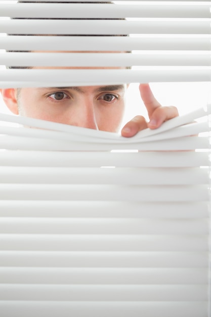 Серьезные мужские глаза шпионируют через рулонные шторы