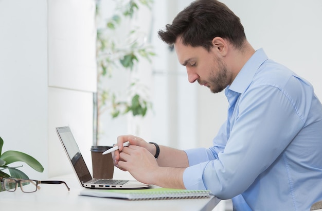 Serious male freelancerlooking at his notebook while working with laptop computer upon business projects in restaurant or cafe