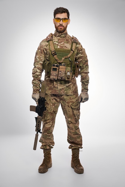 Serious male soldier with rifle in hand posing in studio