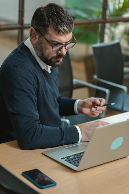 Serious male in stylish wear sitting at table with modern laptop