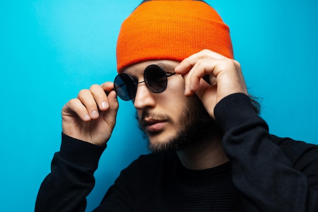 Serious man on blue background Wearing round sunglasses and orange hat