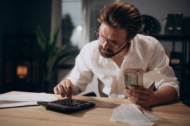 Foto uomo serio che controlla le bollette e conta i soldi in ufficio