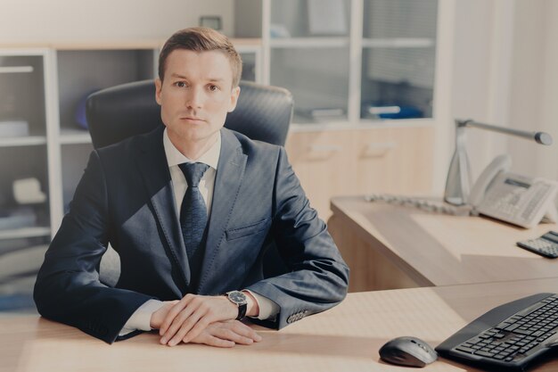 Serious man in formal suit sits at work place in cozy cabinet at office