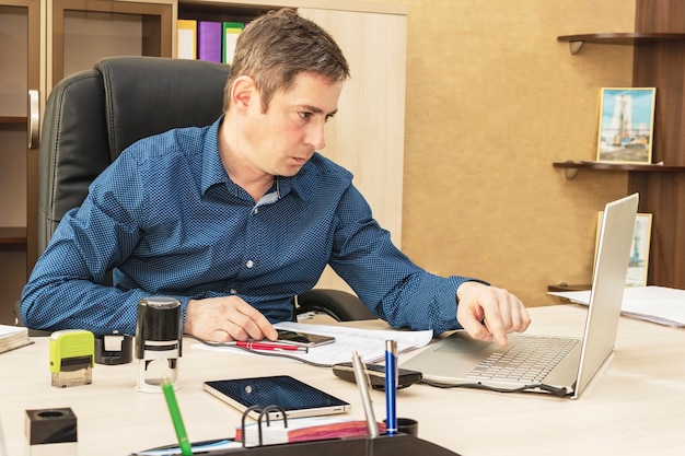 A serious man in his office works at a laptop. Correspondence with business partners. Office worker. Department manager.