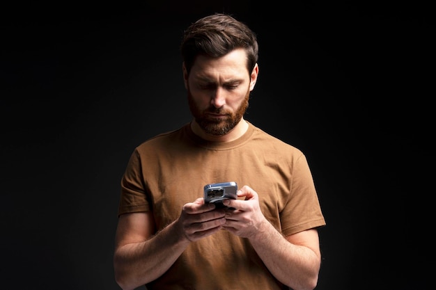 Serious man holding mobile phone text message communication online isolated on black background