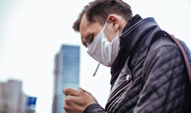 보호 마스크에 심각한 남자가 거리에 서 담배