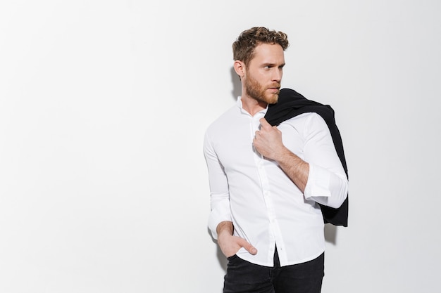 serious man in shirt holding black jacket and looking aside isolated over white wall