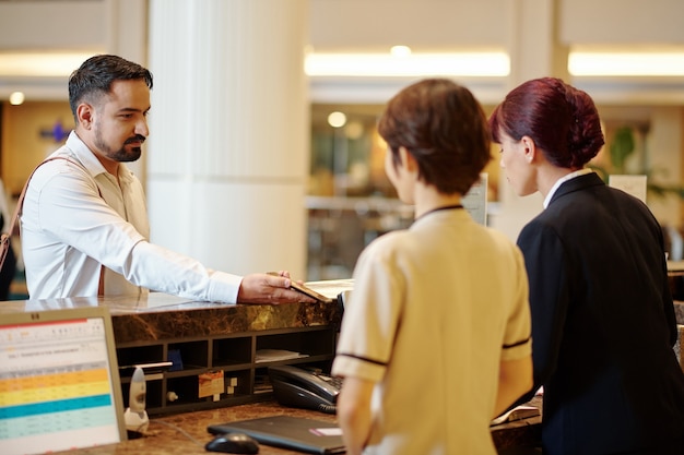 Serious man showing booking information on smartphone to manager at hotel reception