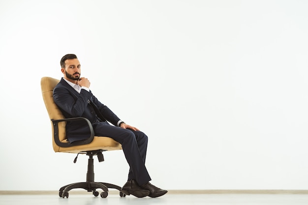 The serious man sitting on an office chair on the white wall background