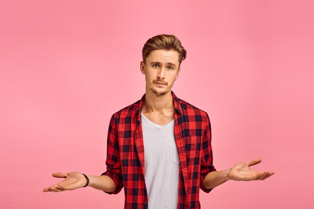 Photo serious man spreads his hands, pink background, emotion