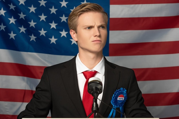 Foto uomo serio sulla tribuna sullo sfondo della bandiera americana