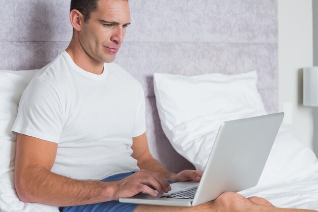 Serious man using laptop on bed