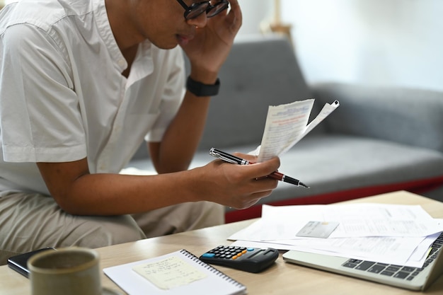 Photo serious man using laptop computer and calculating household expenses