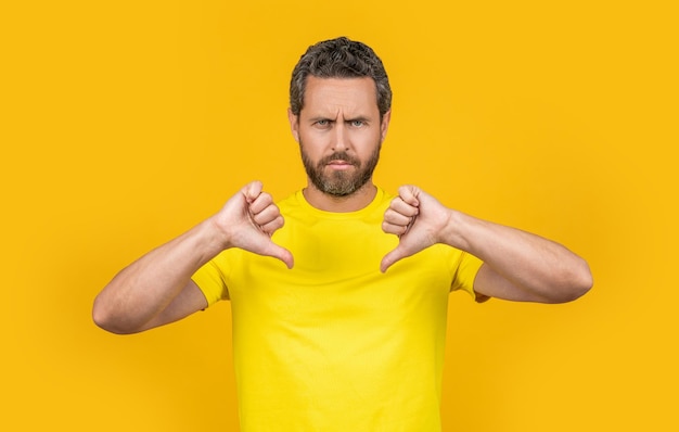 Serious man with dislike gesture on background man with dislike gesture in studio photo of man with dislike gesture thumb down man with dislike gesture isolate on yellow