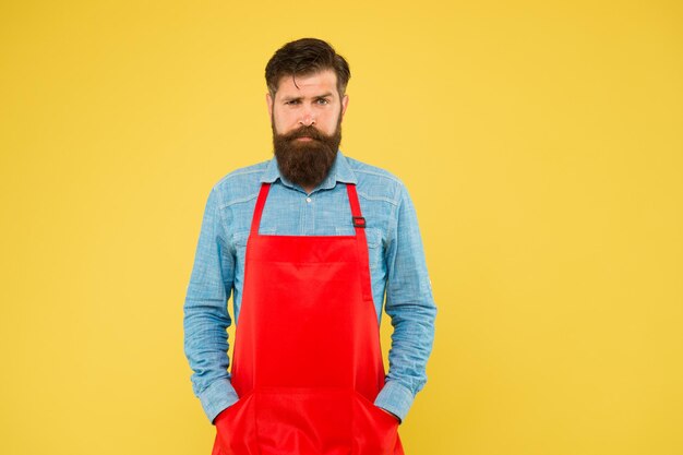 Photo serious man with red apron on yellow background confident expression handsome male barista is working mature bartender his new business guy in shop assistant uniform copy space