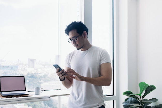 Серьезный человек, работающий с компьютером и телефоном с видом на высотное здание