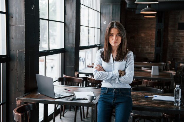 Serious manager. Businesswoman in official clothes is indoors in cafe at daytime.