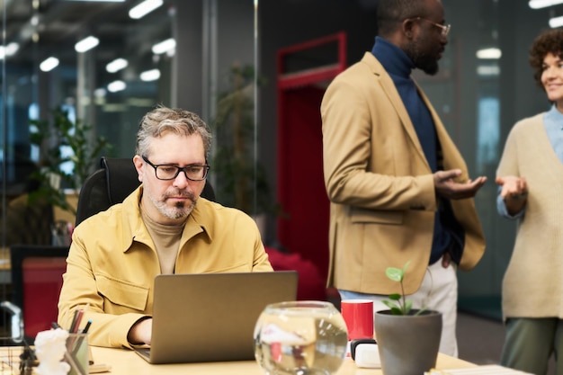 Photo serious mature businessman networking in front of laptop