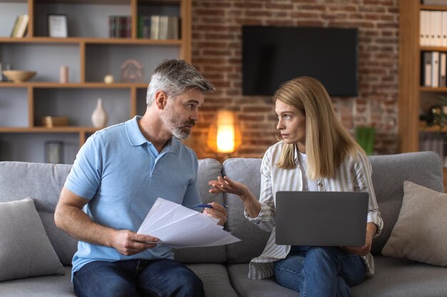 Serious mature caucasian husband and wife work with documents and laptop pay taxes