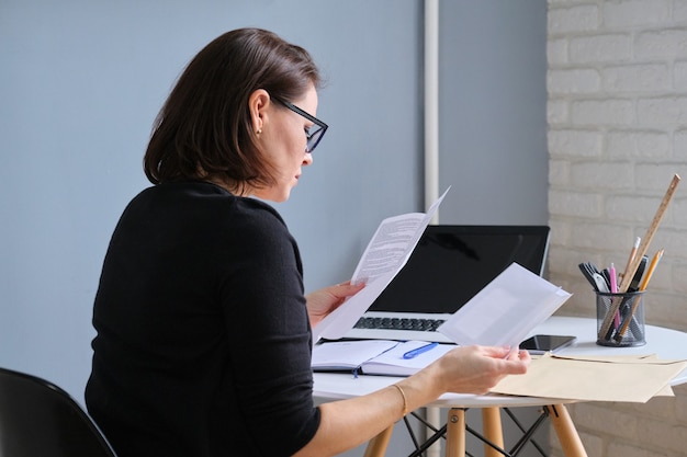 Serious mature woman holding business papers in hands documents received in envelopes by mail