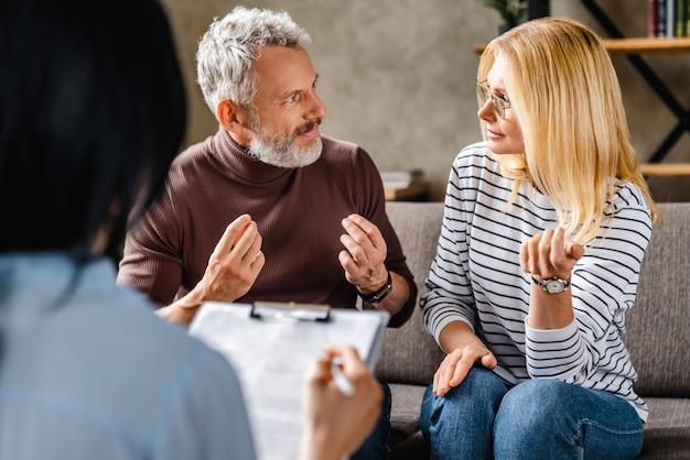 Serious middle aged couple sitting on sofa and discussion with financial advisor at home