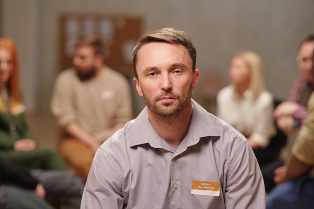 Serious middle aged man sitting against patients of psychologist sharing their problems