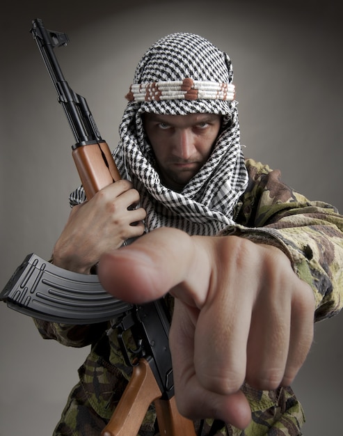 Photo serious middle eastern man with ak-47 pointing to you