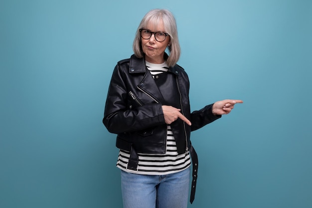 Serious middleaged pensioner woman in gray hair in a stylish youth look on a blue background