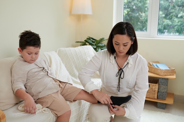 Serious mother or nurse helping child to wear socks