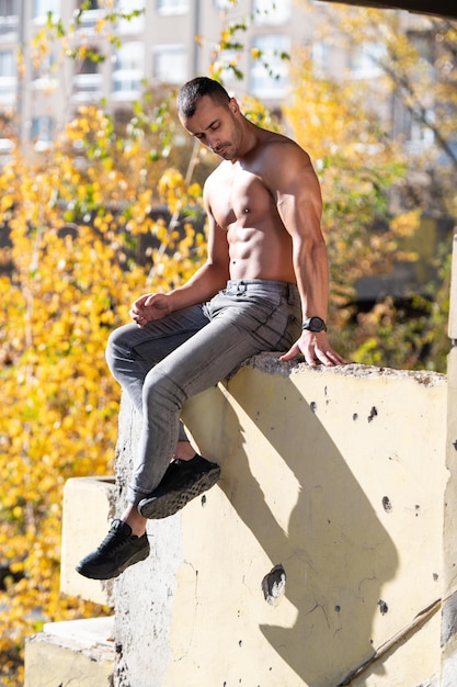 Serious Muscular Model Sitting Outdoors in Ruins