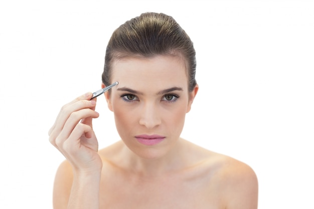 Serious natural brown haired model plucking her eyebrows